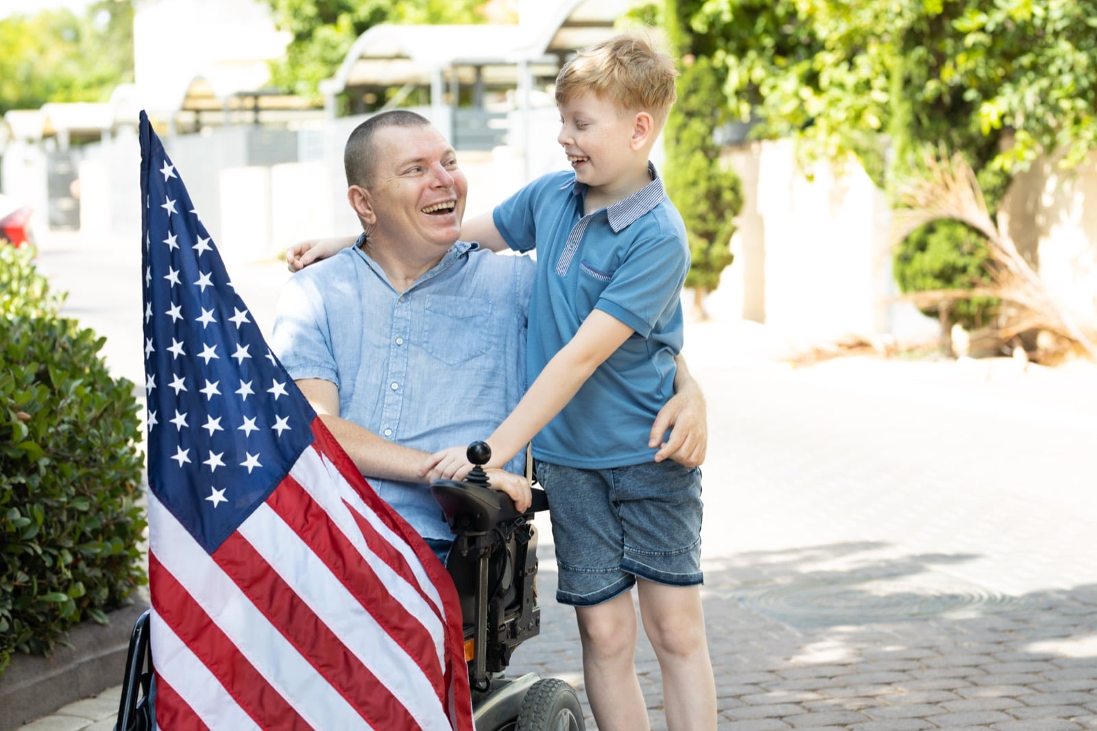 Disabled Veteran in a wheelchair holding an American flag and smiling with his young son