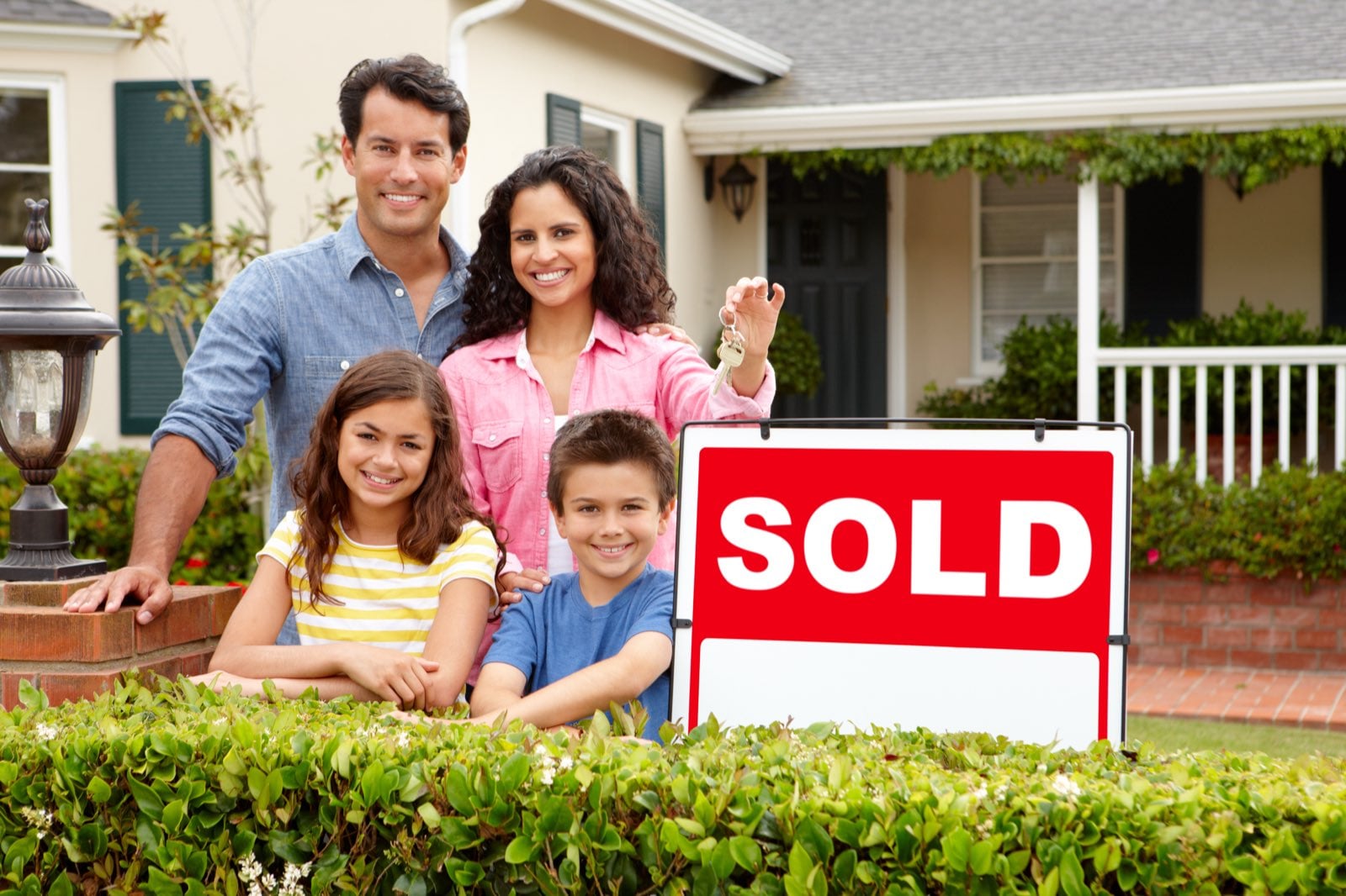Family standing in front of their new home beside a sold sign, holding the keys after getting pre-approved
