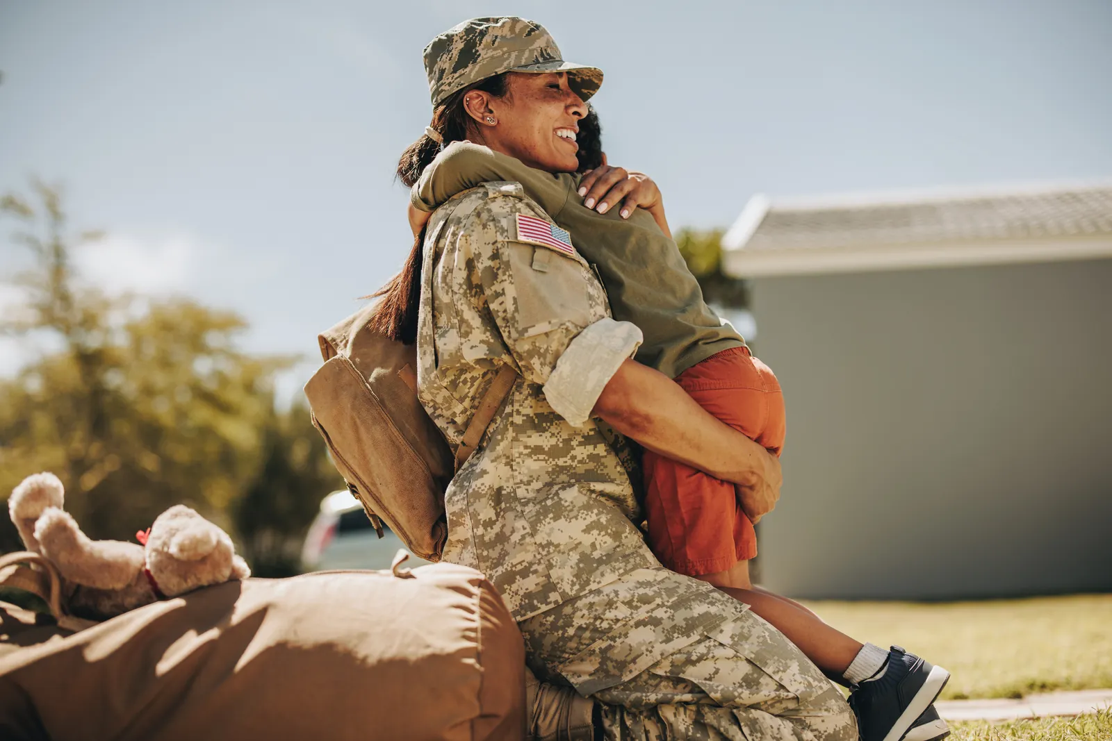 A service member in uniform hugging a child outdoors A service member in uniform hugging a child outdoors