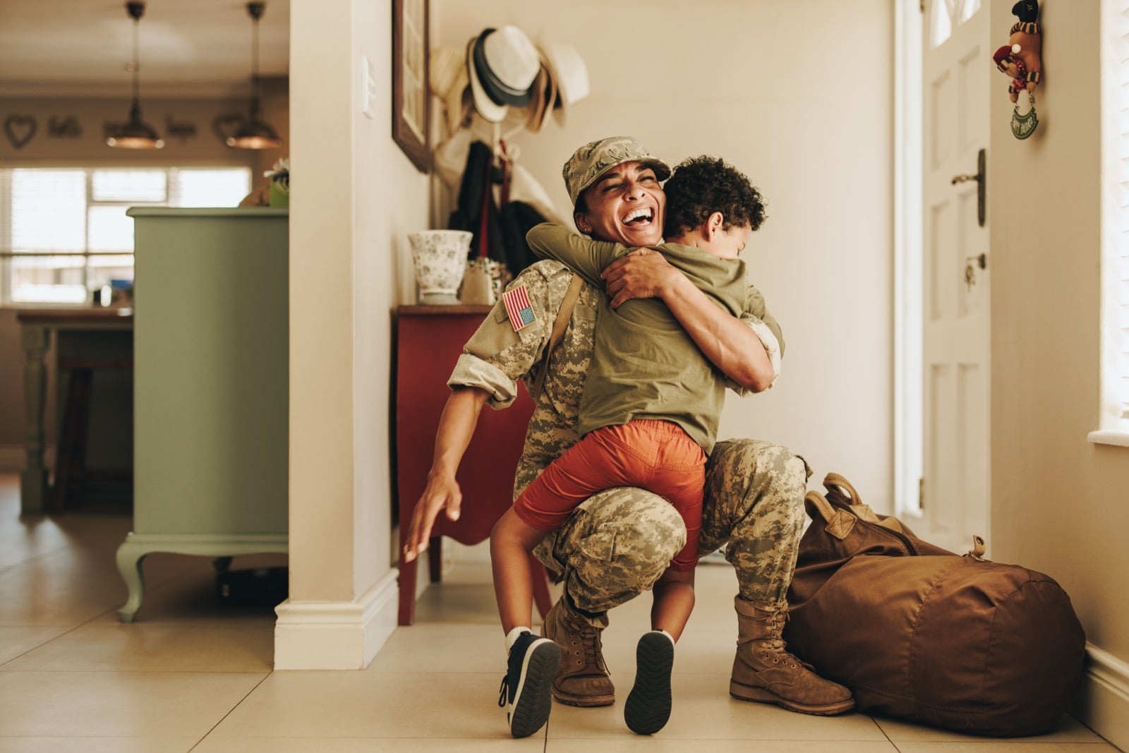 Female service member smiling as she lifts and reunites with her young son at home after deployment