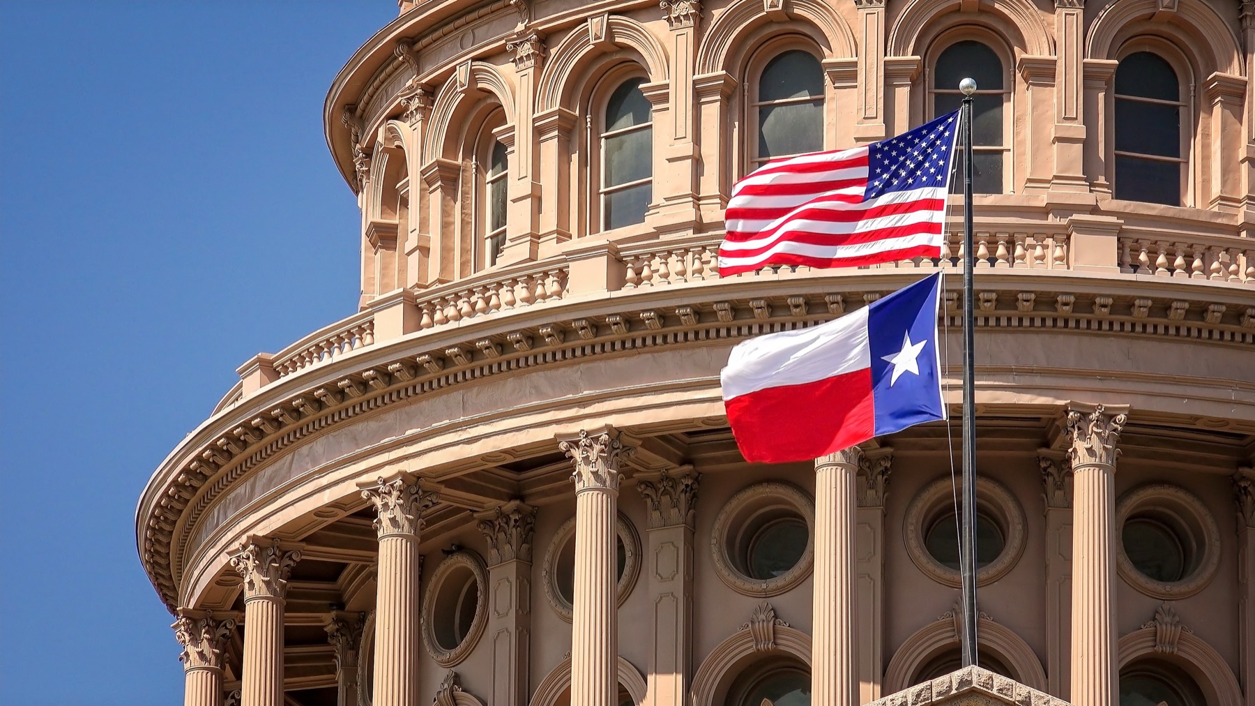 American and Texas flags flying outside the Texas State Capitol in Austin