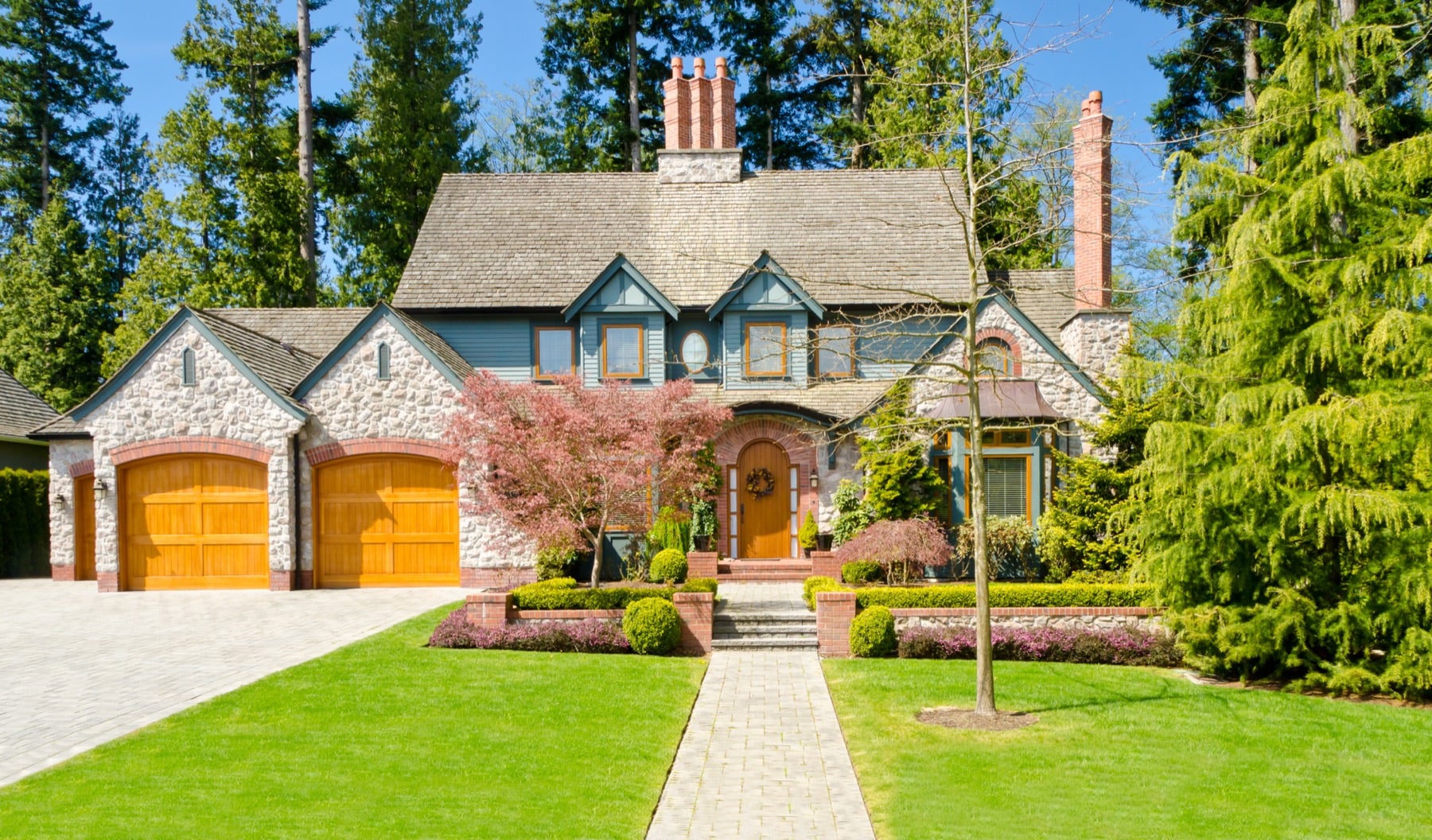 Large stone-and-timber luxury home with mature landscaping and a three-car garage